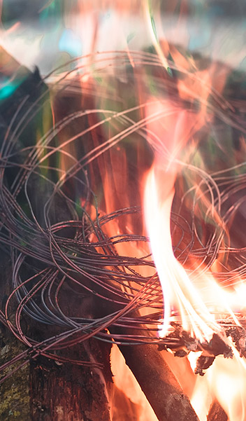 A close-up of coiled metal wires placed over a burning fire, at a copper recycling plant
