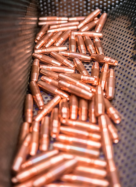 A collection of shiny, copper-colored bullet casings lying on a perforated metal surface inside an industrial container in Bahrain.